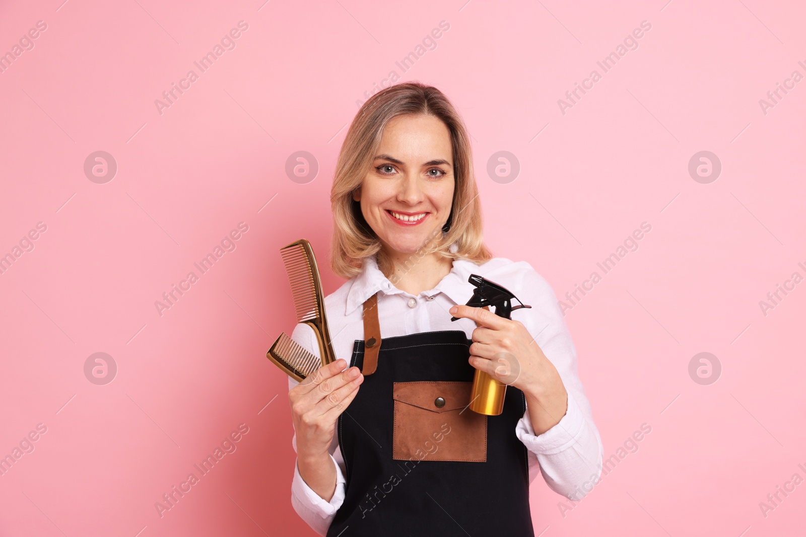 Photo of Smiling hairdresser with combs and spray bottle on pink background