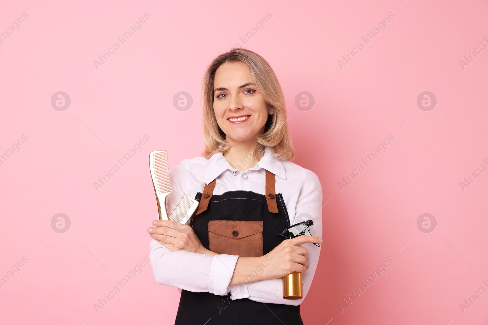 Photo of Smiling hairdresser with combs and spray bottle on pink background