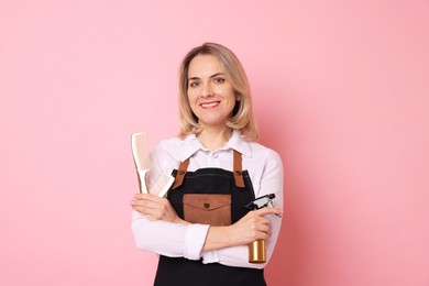 Photo of Smiling hairdresser with combs and spray bottle on pink background