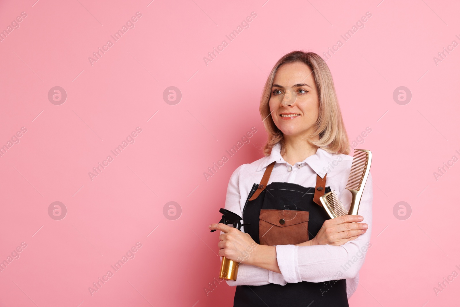 Photo of Smiling hairdresser with combs and spray bottle on pink background, space for text