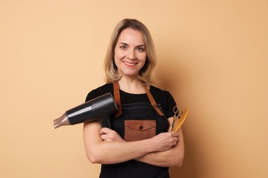 Photo of Smiling hairdresser with dryer, scissors and comb on beige background