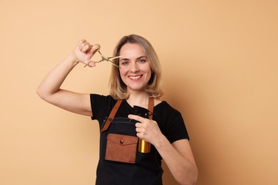 Photo of Smiling hairdresser with scissors and spray bottle on beige background