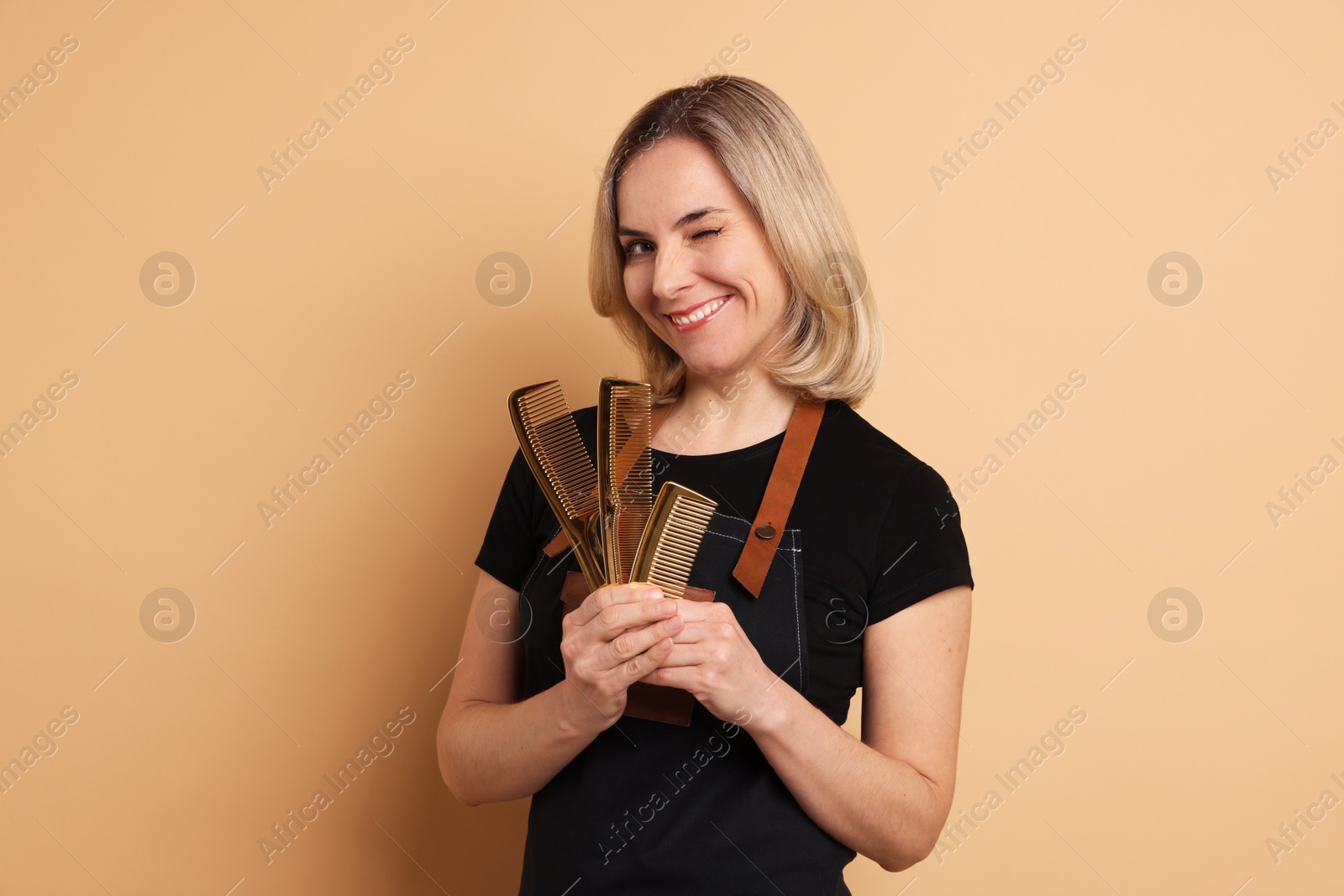 Photo of Smiling hairdresser with combs on beige background