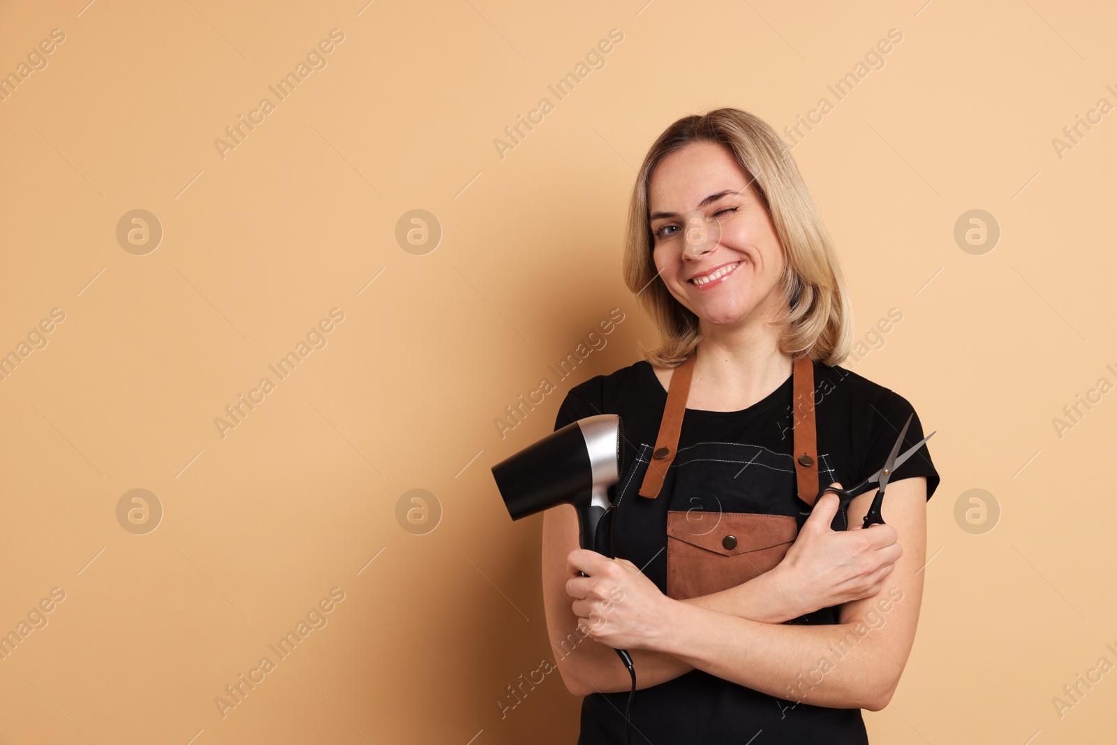 Photo of Smiling hairdresser with dryer and scissors on beige background, space for text