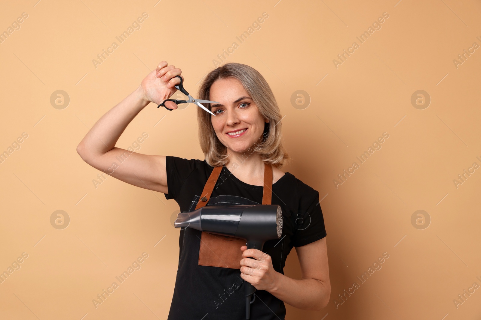 Photo of Smiling hairdresser with dryer and scissors on beige background