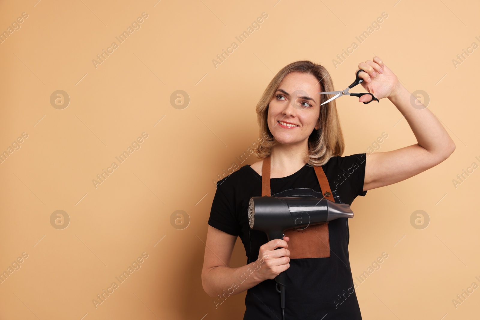 Photo of Smiling hairdresser with dryer and scissors on beige background, space for text