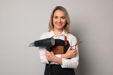 Smiling hairdresser with dryer and scissors on gray background