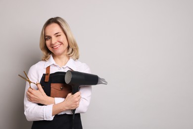 Smiling hairdresser with dryer and scissors on gray background, space for text