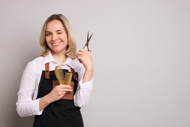 Photo of Smiling hairdresser with scissors and combs on gray background, space for text