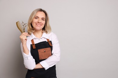 Smiling hairdresser with scissors and comb on gray background, space for text