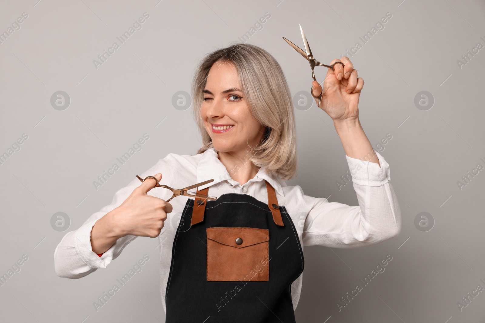 Photo of Smiling hairdresser with scissors on gray background