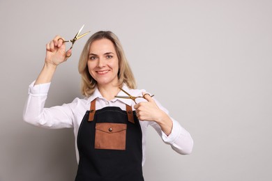 Smiling hairdresser with scissors on gray background, space for text