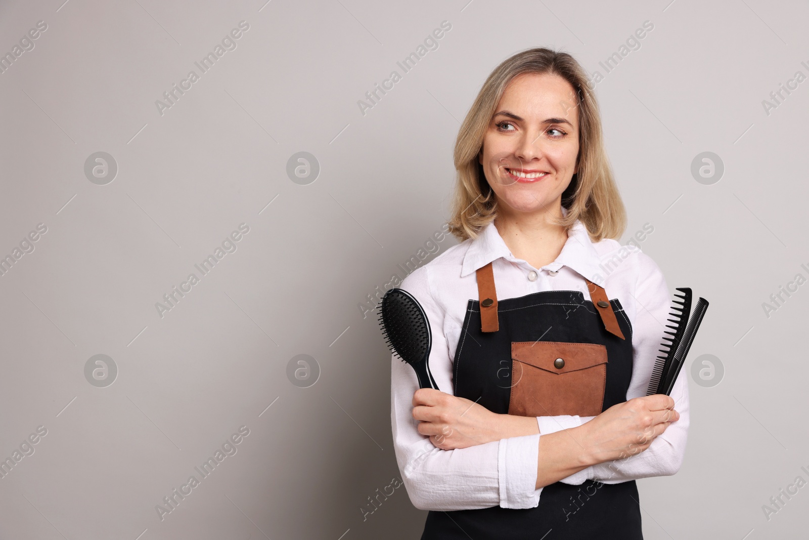 Photo of Smiling hairdresser with combs and brush on gray background, space for text