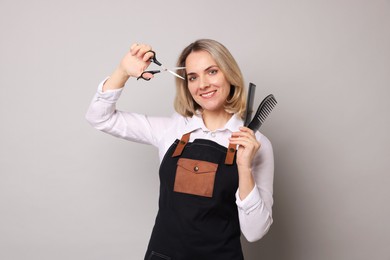 Photo of Smiling hairdresser with combs and brush on gray background