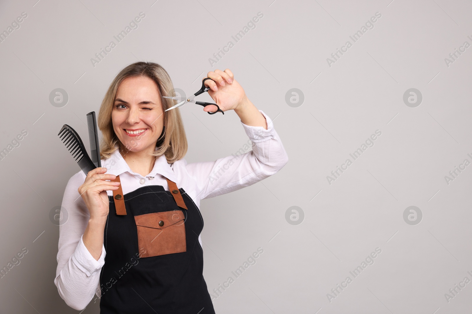 Photo of Smiling hairdresser with combs and brush on gray background, space for text