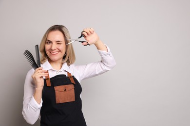 Smiling hairdresser with combs and brush on gray background, space for text