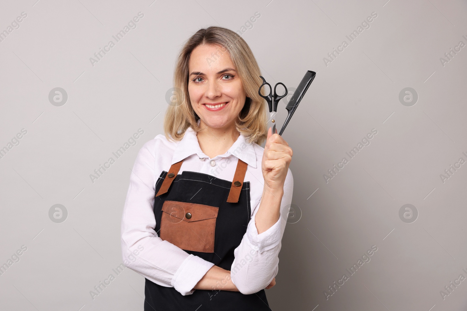 Photo of Smiling hairdresser with comb and scissors on gray background