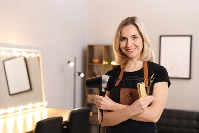 Photo of Hairdresser with dryer, comb and scissors in beauty salon, space for text