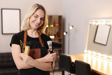 Hairdresser with dryer, comb and scissors in beauty salon, space for text