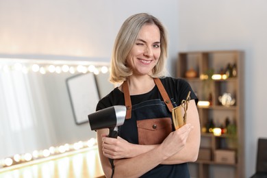 Photo of Hairdresser with dryer, comb and scissors in beauty salon