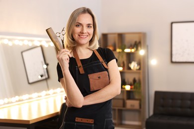 Photo of Smiling hairdresser with scissors and comb in beauty salon