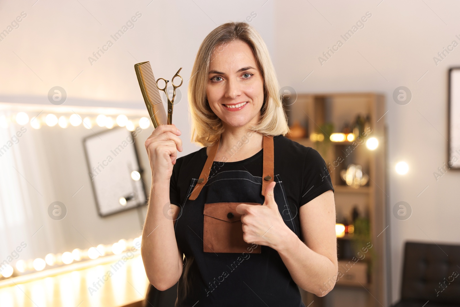 Photo of Smiling hairdresser with scissors and comb showing thumbs up in beauty salon