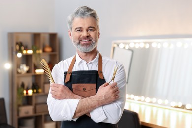 Photo of Smiling hairdresser with scissors and comb in beauty salon