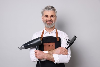 Photo of Smiling hairdresser with dryer, scissors and comb on gray background