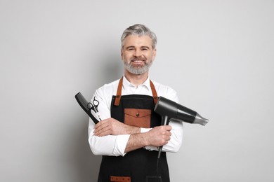 Photo of Smiling hairdresser with dryer, scissors and comb on gray background