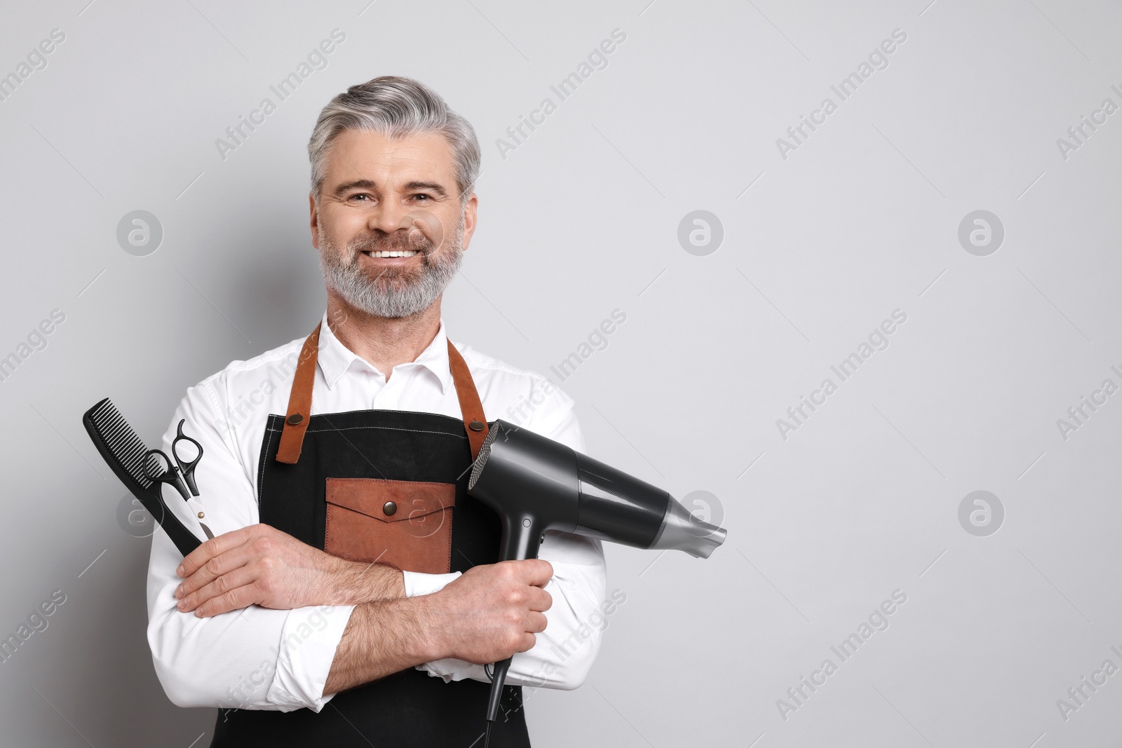 Photo of Smiling hairdresser with dryer, scissors and comb on gray background, space for text