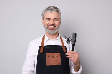 Smiling hairdresser with scissors and comb on gray background