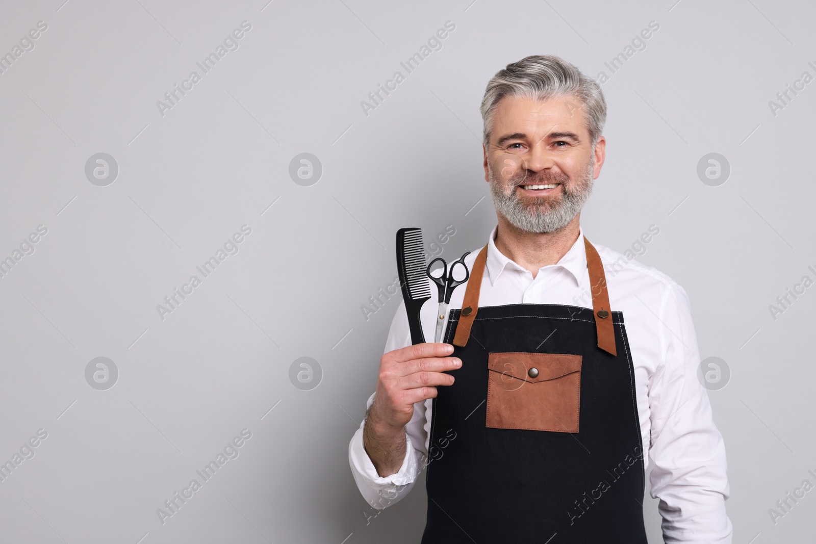 Photo of Smiling hairdresser with scissors and comb on gray background, space for text