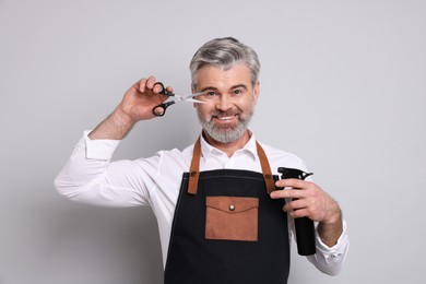 Smiling hairdresser with scissors and spray bottle on gray background