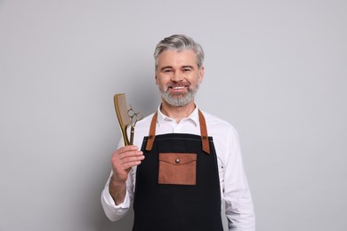 Photo of Smiling hairdresser with scissors and comb on gray background