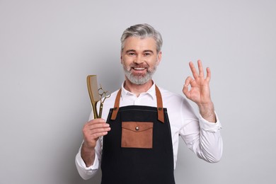 Photo of Smiling hairdresser with scissors and comb showing OK gesture on gray background