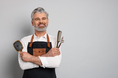 Smiling hairdresser with scissors, comb and brush on gray background, space for text