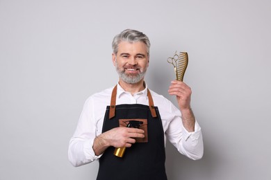 Photo of Smiling hairdresser with scissors, comb and spray bottle on gray background