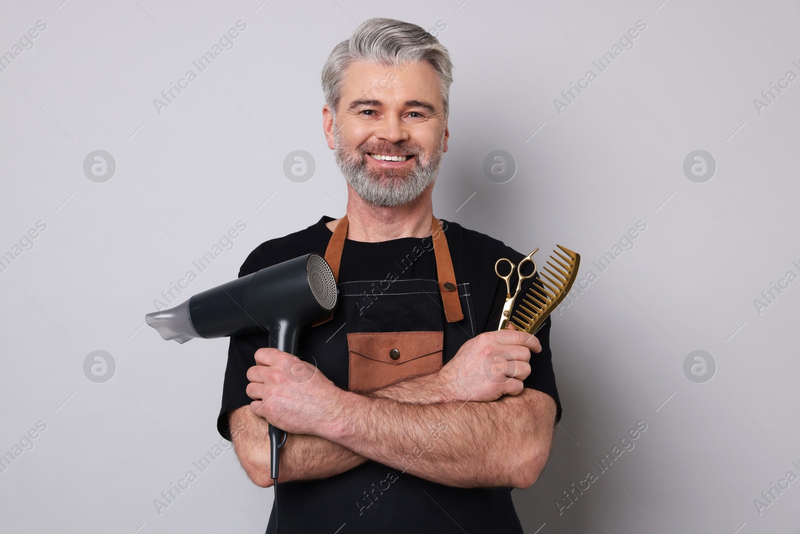 Photo of Smiling hairdresser with dryer, scissors and comb on gray background