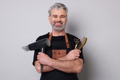 Photo of Smiling hairdresser with dryer, scissors and comb on gray background