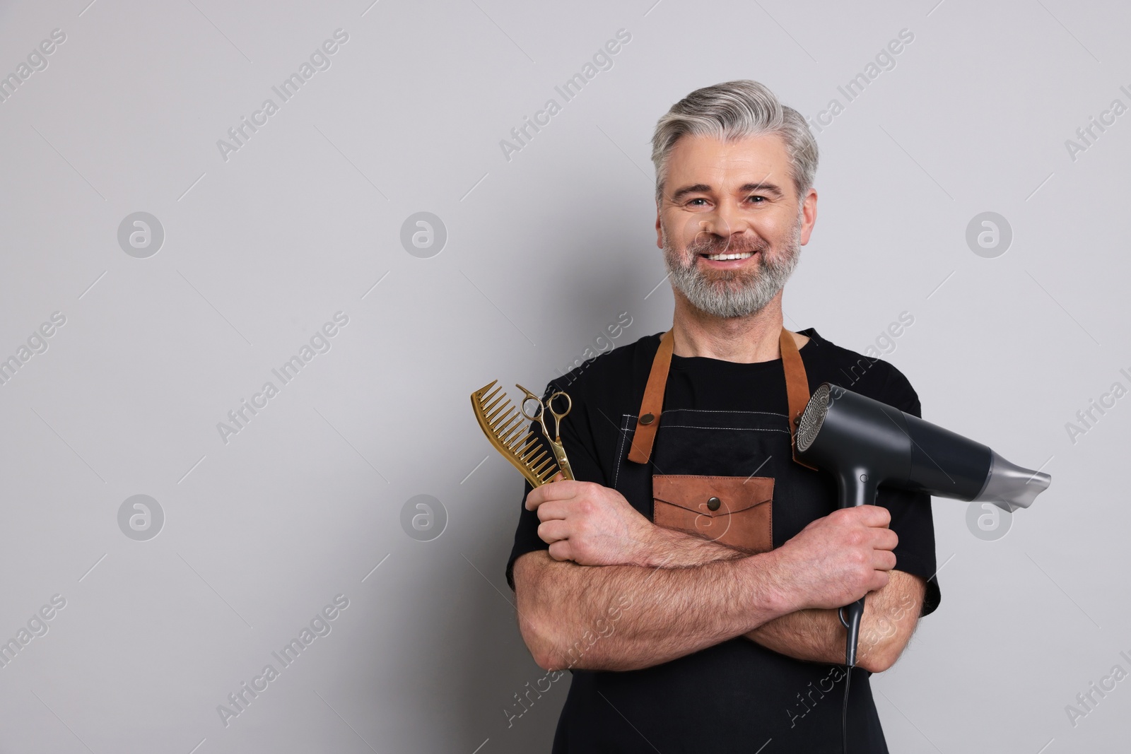 Photo of Smiling hairdresser with dryer, scissors and comb on gray background, space for text