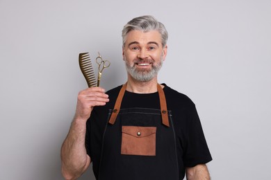 Photo of Smiling hairdresser with scissors and comb on gray background