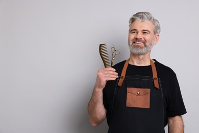 Photo of Smiling hairdresser with scissors and comb on gray background, space for text