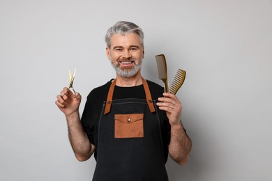 Photo of Smiling hairdresser with scissors and combs on gray background