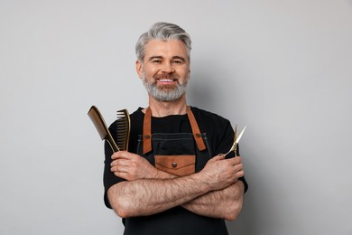 Smiling hairdresser with scissors and combs on gray background