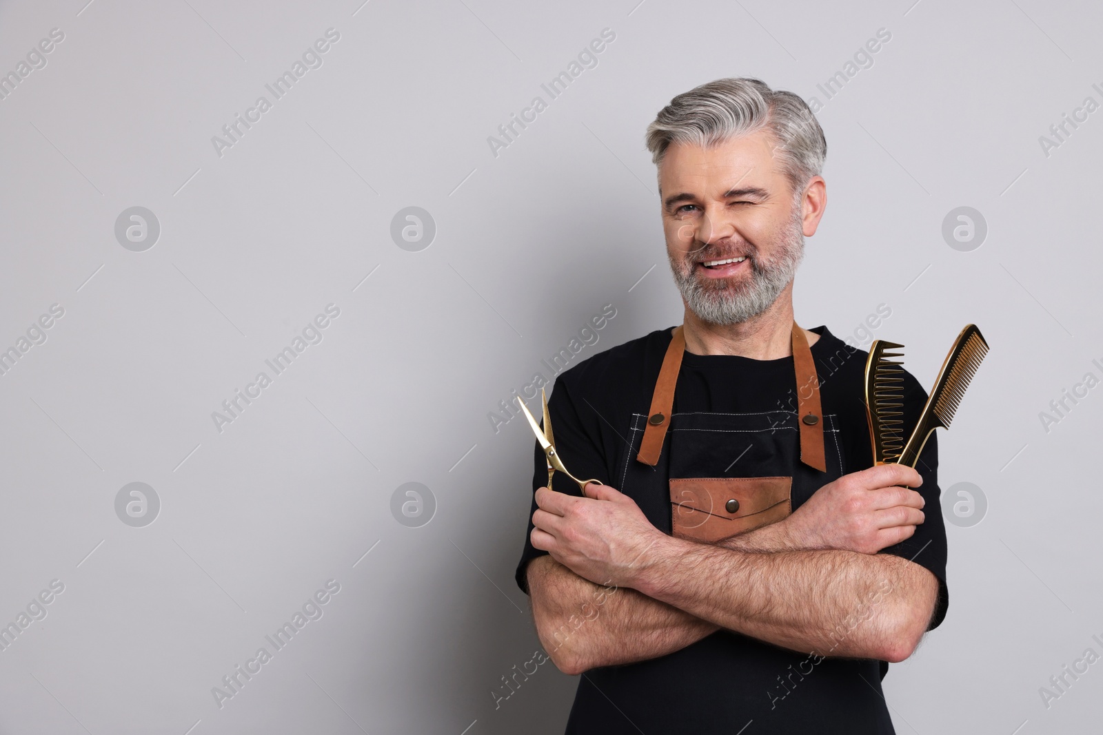 Photo of Smiling hairdresser with scissors and combs on gray background, space for text