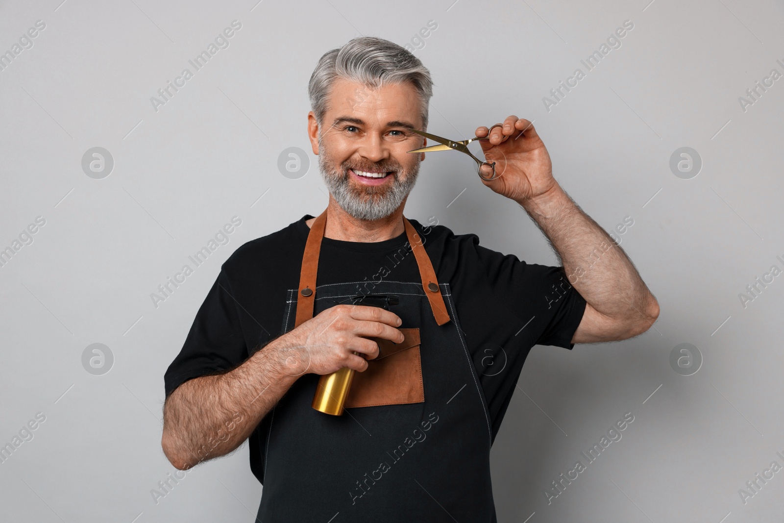 Photo of Smiling hairdresser with scissors and spray bottle on gray background