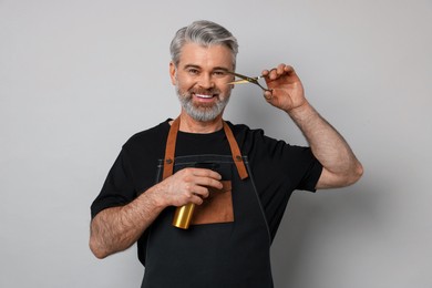 Smiling hairdresser with scissors and spray bottle on gray background