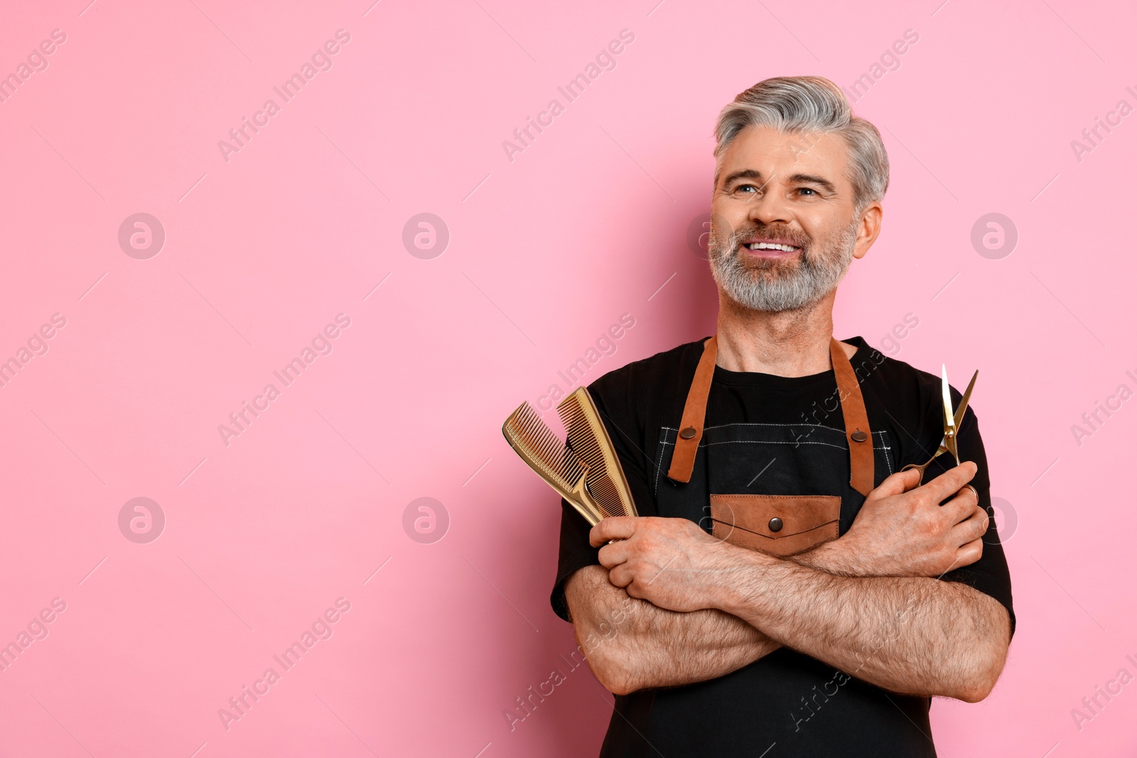 Photo of Smiling hairdresser with scissors and combs on pink background, space for text