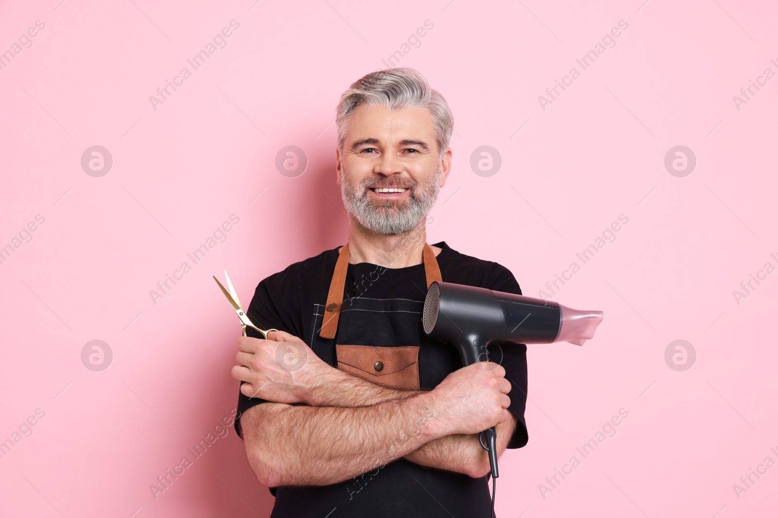 Photo of Smiling hairdresser with dryer and scissors on pink background