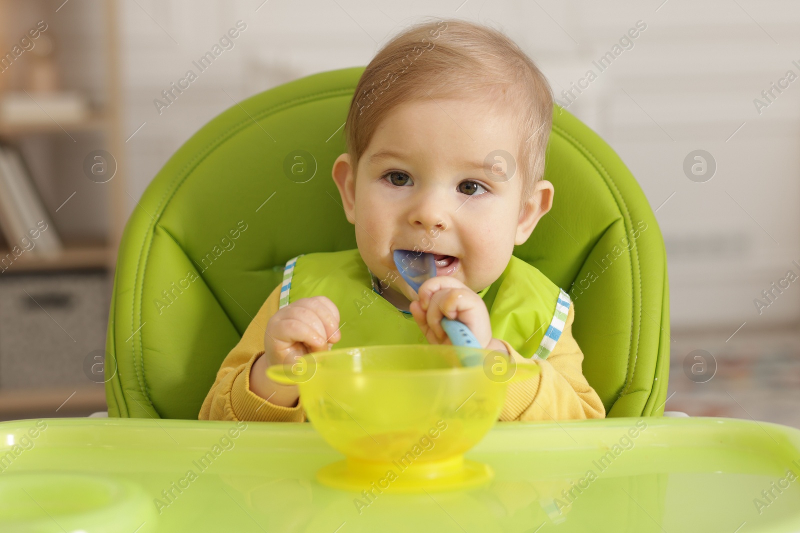 Photo of Cute little baby eating healthy food in high chair indoors